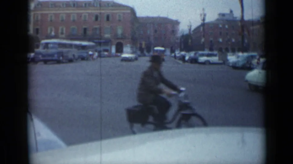 A motorcycle or scooter rider passes close to the camera in the 1962 Cannes traffic scene, with cars and a bus beyond.