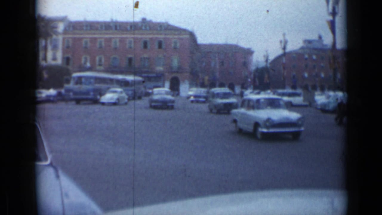 Cannes traffic scene with mid-century cars entering the roadway, a blue bus, sidewalks, and multi-story buildings.