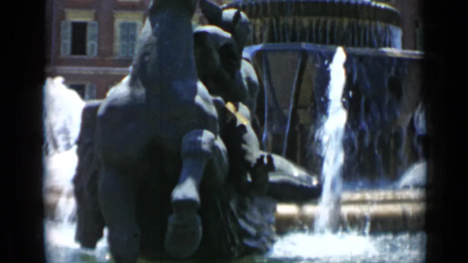1962 Cannes 8mm frame showing a close tourist view of the horse sculpture beside the fountain's falling water.