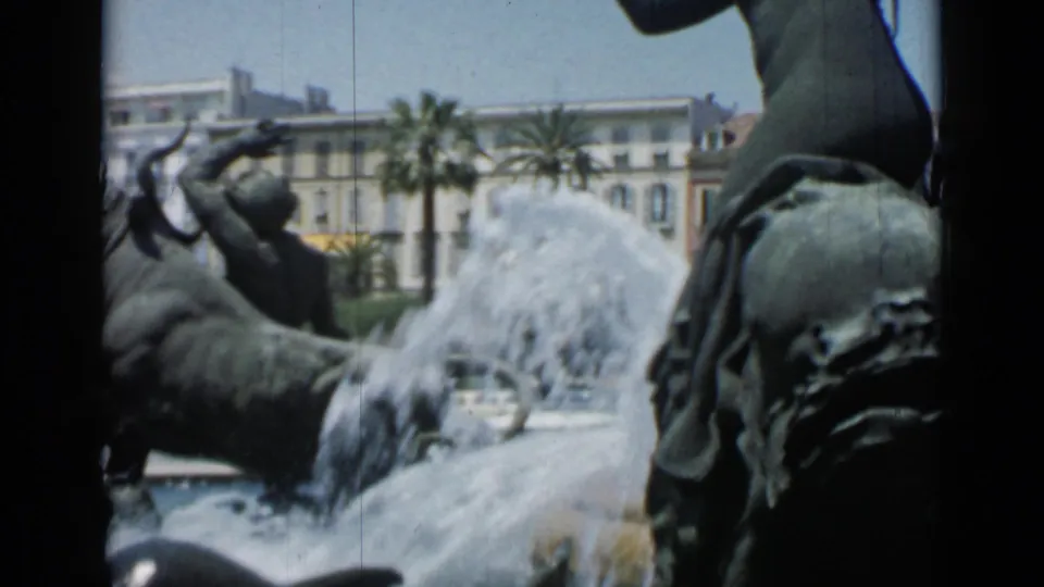 Cannes 1962 8mm frame of animal and human fountain sculptures with a strong water plume and boulevard scenery behind.