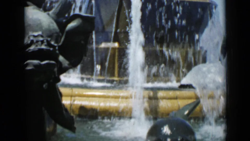 1962 Cannes 8mm frame showing fountain water cascading past dark sculptural figures and a pale statue base.