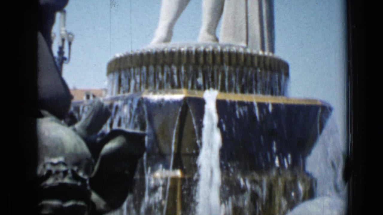 Fountain tiers with cascading water below the lower body of a pale statue.