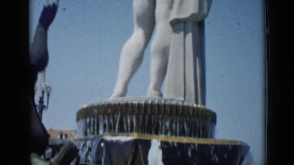 1962 Cannes 8mm view of a classical nude statue above a cascading public fountain against blue sky.
