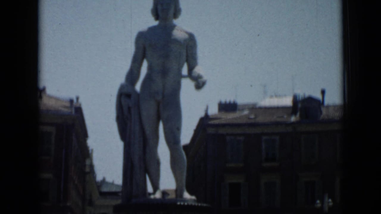 Front view of the standing statue above city buildings under a pale blue sky.