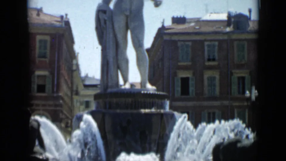 Wider 1962 Cannes view showing the statue on its fountain basin, water jets, and surrounding multi-story buildings.