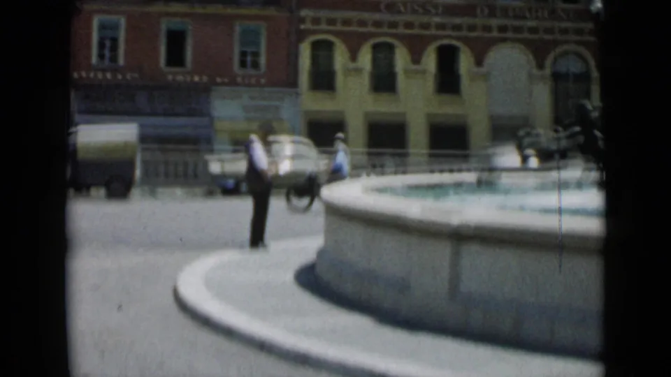 A Cannes street view shows a man by the fountain, pedestrians, a small cart or vehicle, and storefronts behind him.