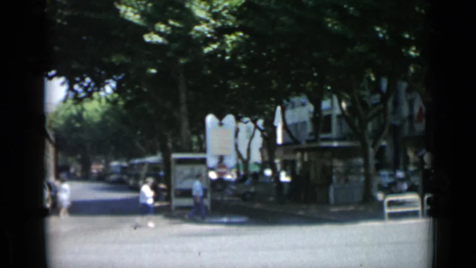 1962 Cannes boulevard view with pedestrians moving under shade trees near street signs, storefronts, and parked cars.