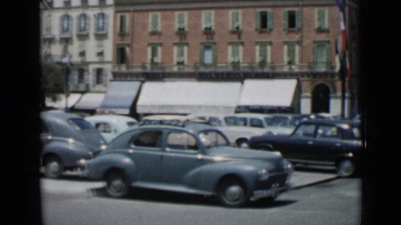 Sunlit Cannes street with classic cars, shuttered buildings, awnings, and a pale blue sedan in the foreground.