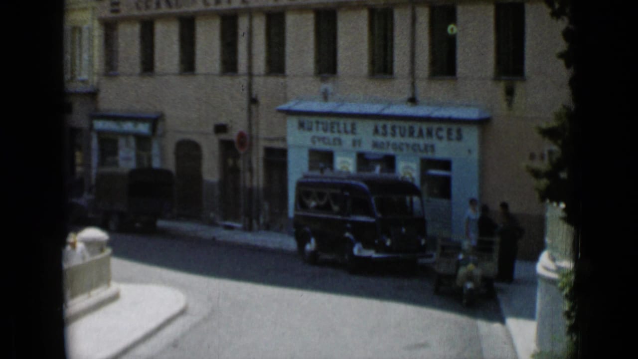 French storefront reading MUTUELLE ASSURANCES with a dark van, pedestrians, and a narrow street corner.