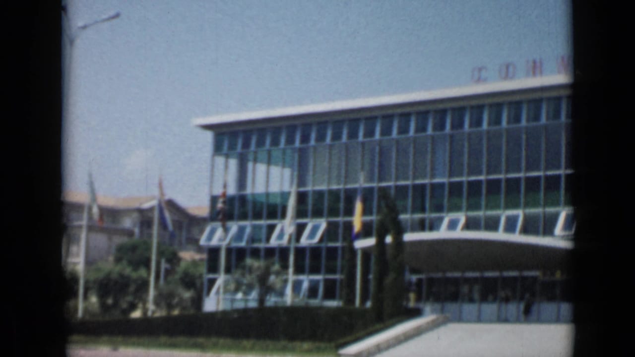 Modern glass convention building with flagpoles and partial rooftop lettering.