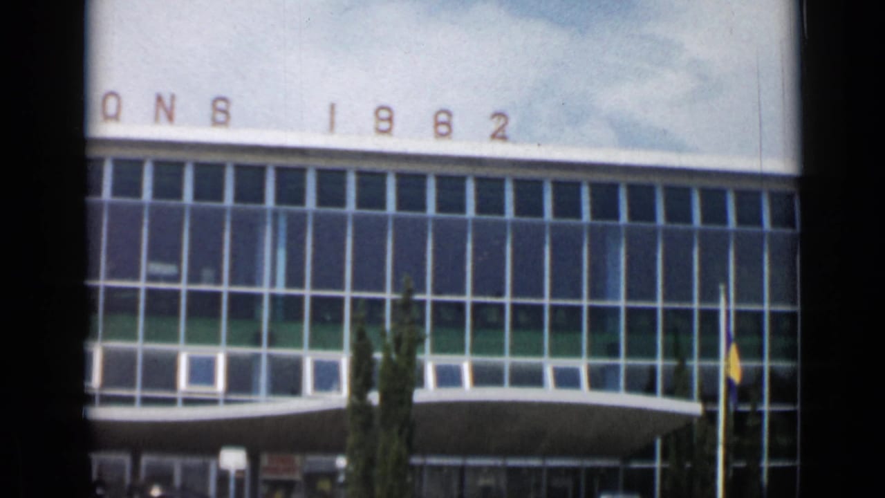 Modern glass facade with LIONS 1962 lettering, flagpole, cypress tree, and entrance area.