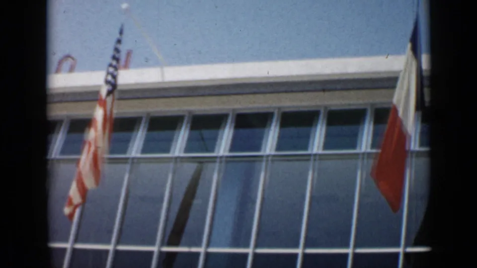 1962 Cannes frame with the American flag at left and a French flag entering at right before the glass facade.