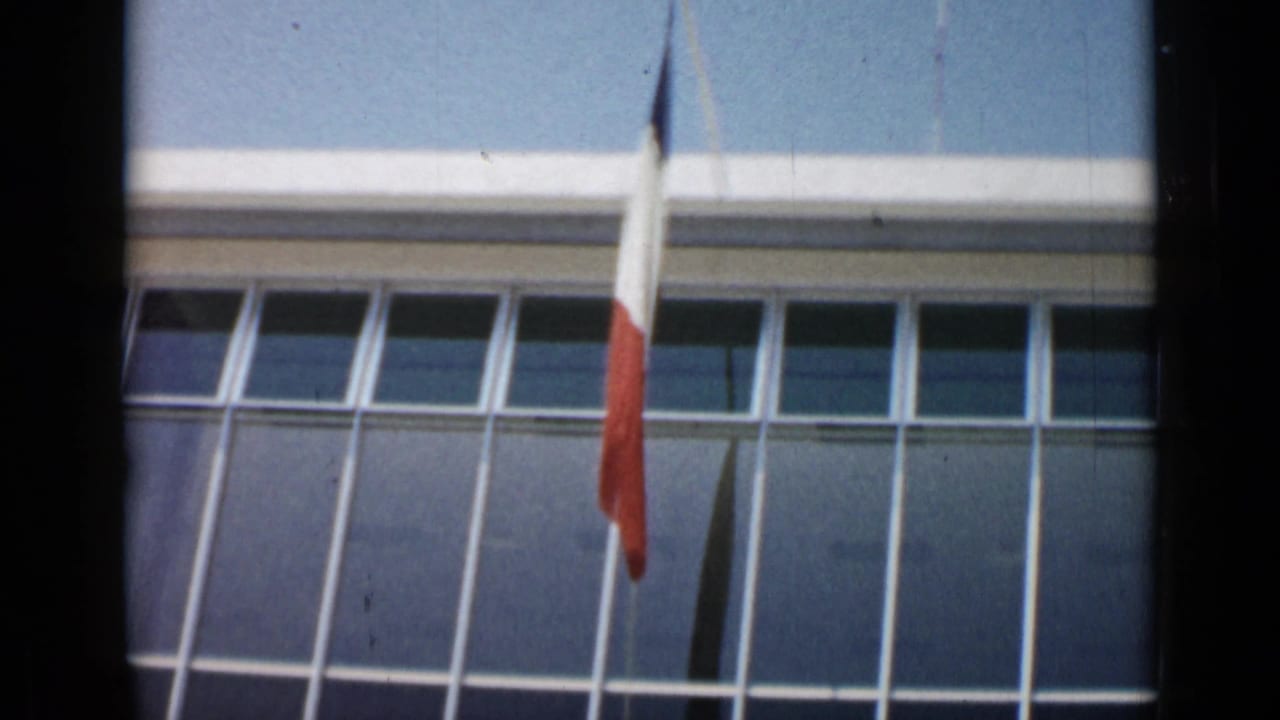 French tricolor flag in front of a modern glass-fronted building.