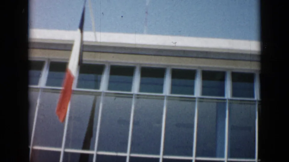 French tricolor seen against a glass-fronted building facade in Cannes, France, in early-1960s home-movie footage.