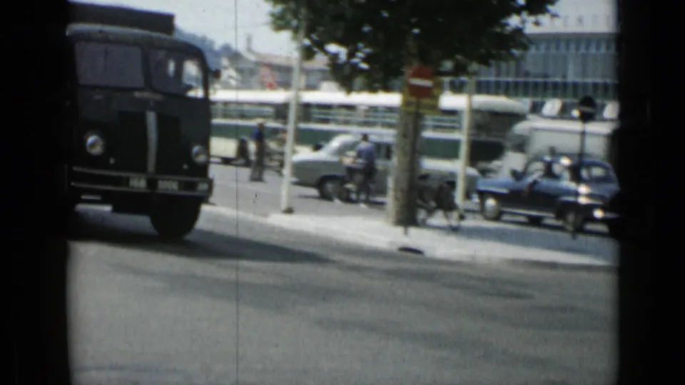 Cannes street view with parked and moving mid-century vehicles, pedestrians, and a dark truck crossing the frame.