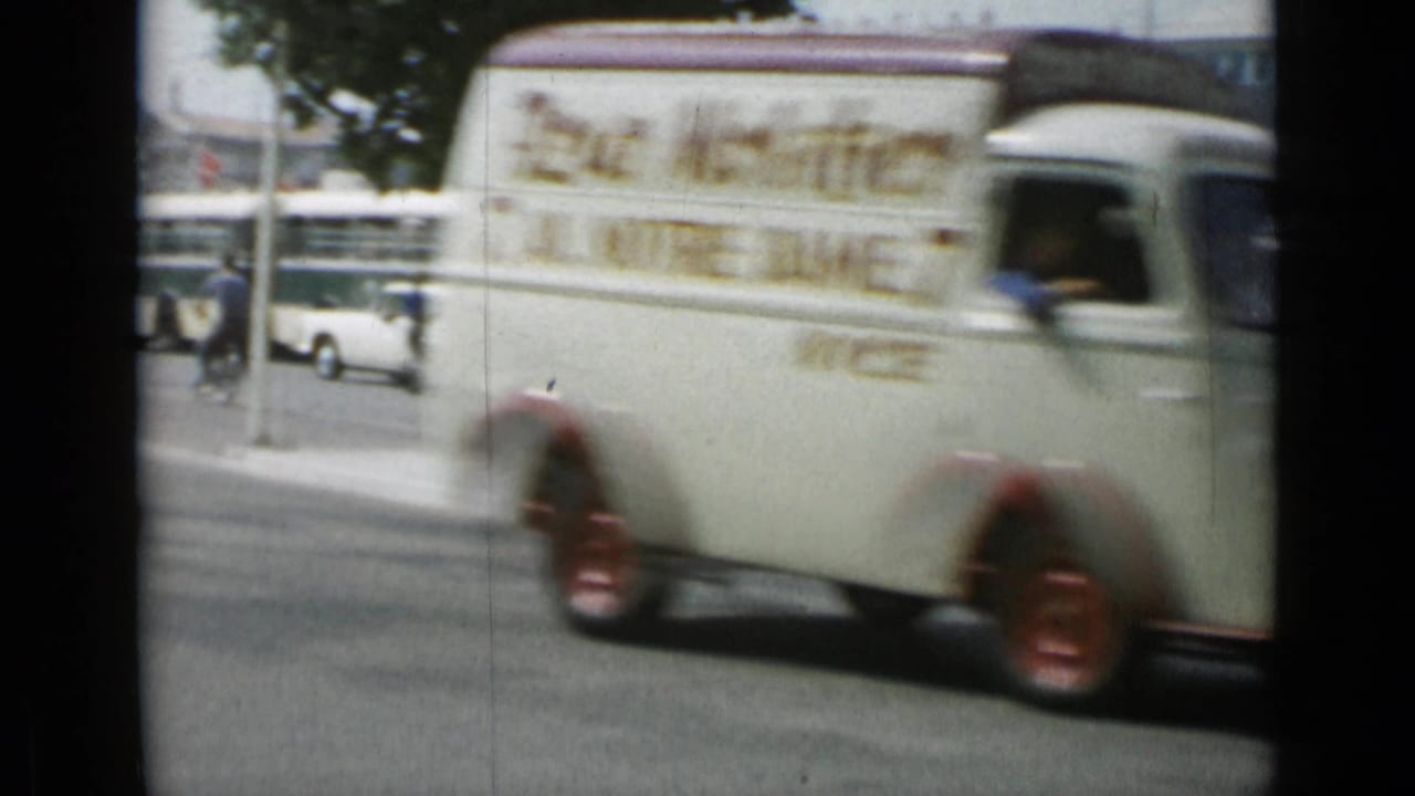 White delivery van with red wheels driving past street traffic.