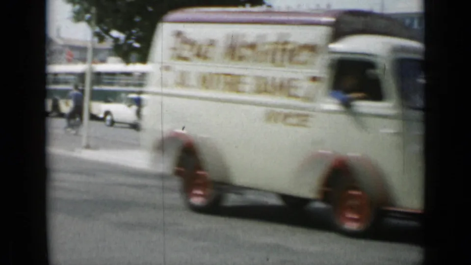 A white delivery van with red wheels passes through Cannes street traffic in the supplied 1962 footage.