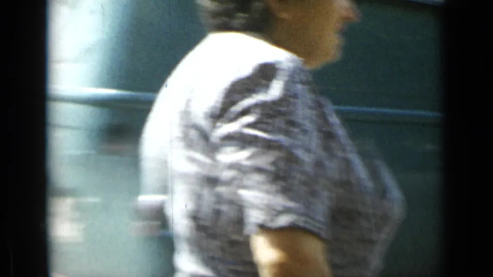 A passerby in patterned clothing crosses close to the 8mm camera, partially obscuring the Cannes street scene with motion blur.