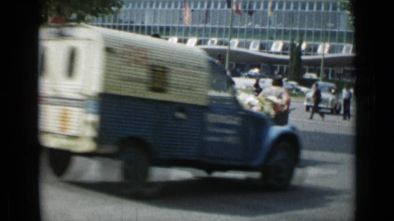 Blue-and-white delivery van drives past pedestrians and traffic.
