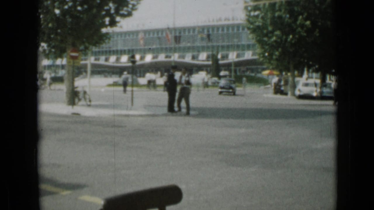 Cannes street intersection with pedestrians, cars, trees, and a glass-fronted building.