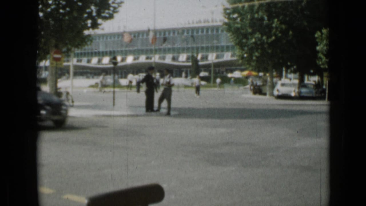 Street outside a modern building with pedestrians, trees, and a car at the curb.