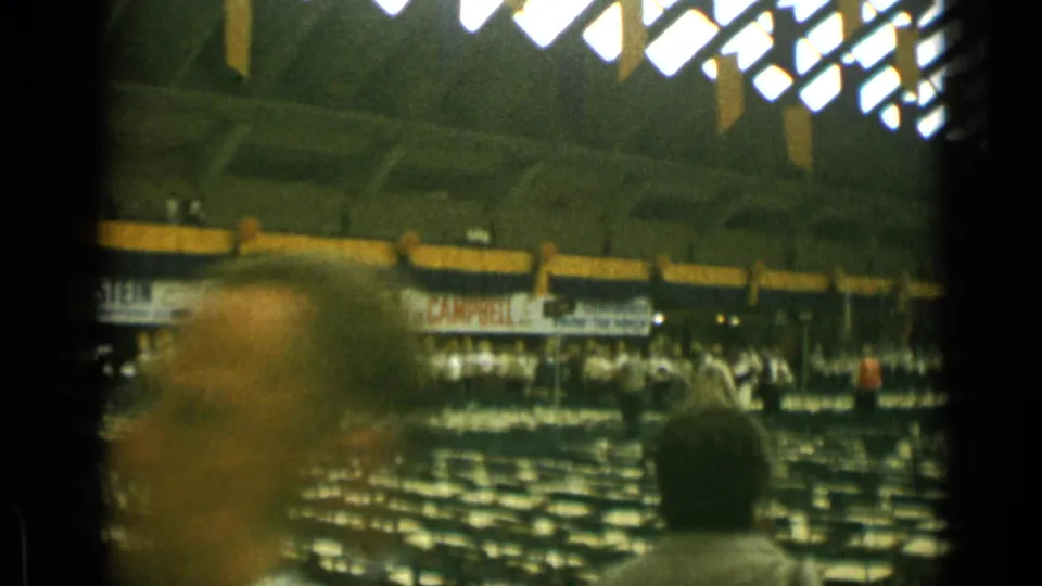 Indoor auditorium in the Cannes 1962 clip, showing many empty seats, scattered attendees, banners, and bright overhead lighting.
