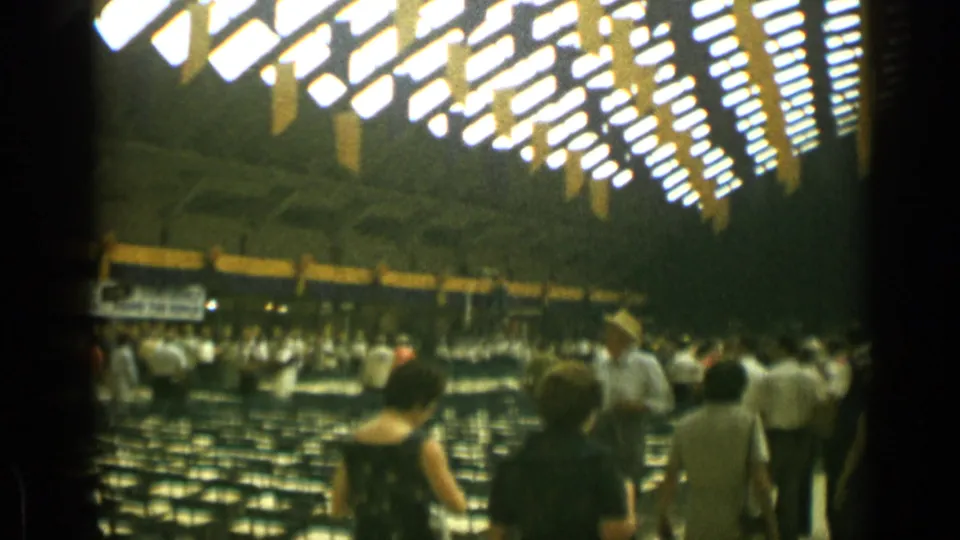 Crowd inside a Cannes auditorium, with men and women walking past empty seating under rows of bright overhead lights.