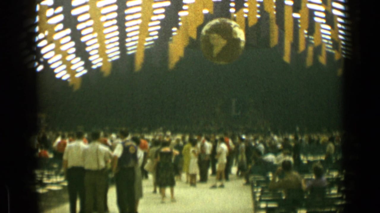 Crowd gathered in a large hall beneath ceiling lights and a hanging globe.