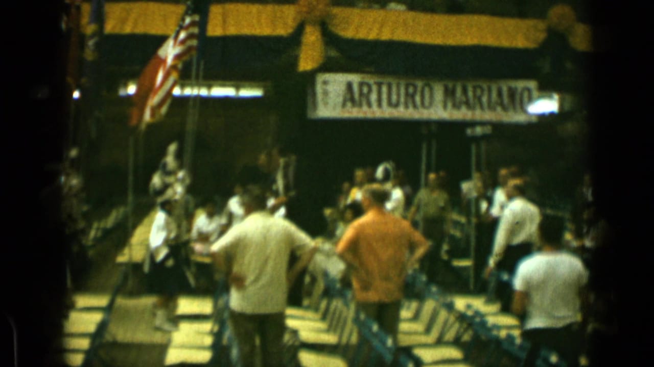 1962 Cannes frame showing men near flags and an Arturo Mariano banner during an indoor public gathering.