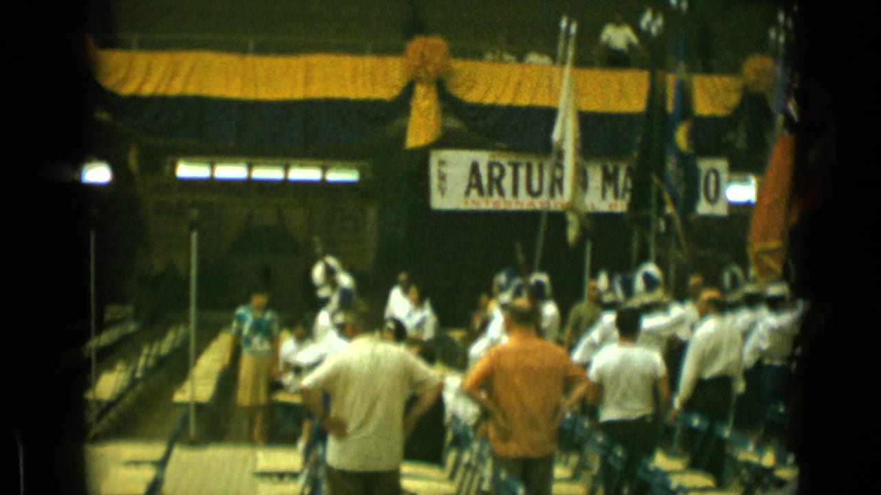 Adults watch white-uniformed musicians on a decorated platform with a banner overhead.