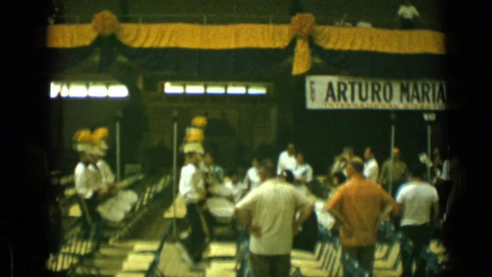 White-uniformed percussion players with tall yellow headwear appear on the decorated Cannes platform while adults watch from the foreground.