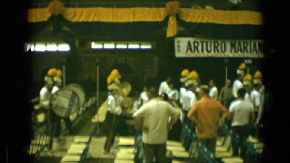 Cannes, France, 1962 home-movie frame showing uniformed band members with yellow plumes playing near spectators and draped decor.