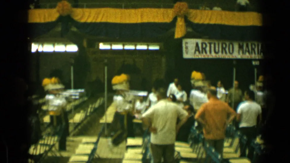 Cannes, France, 1962 home-movie frame of a band performance with spectators, folding chairs, drapery, and a visible background banner.