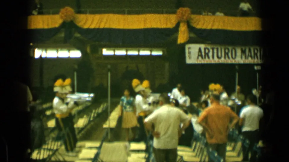 1962 Cannes frame showing a marching band performer with yellow plume crossing in front of audience seating.
