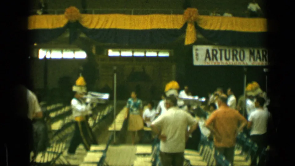 1962 Cannes home-movie view of band members with yellow plumes performing beneath stage decorations and signage.