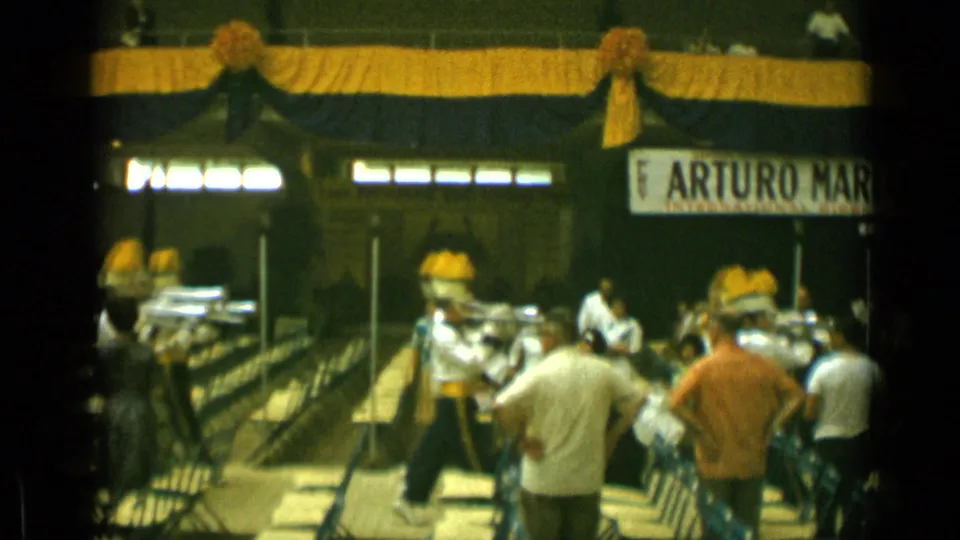 1962 Cannes home-movie frame showing uniformed band members with yellow plumes performing near spectators and a decorated stage area.