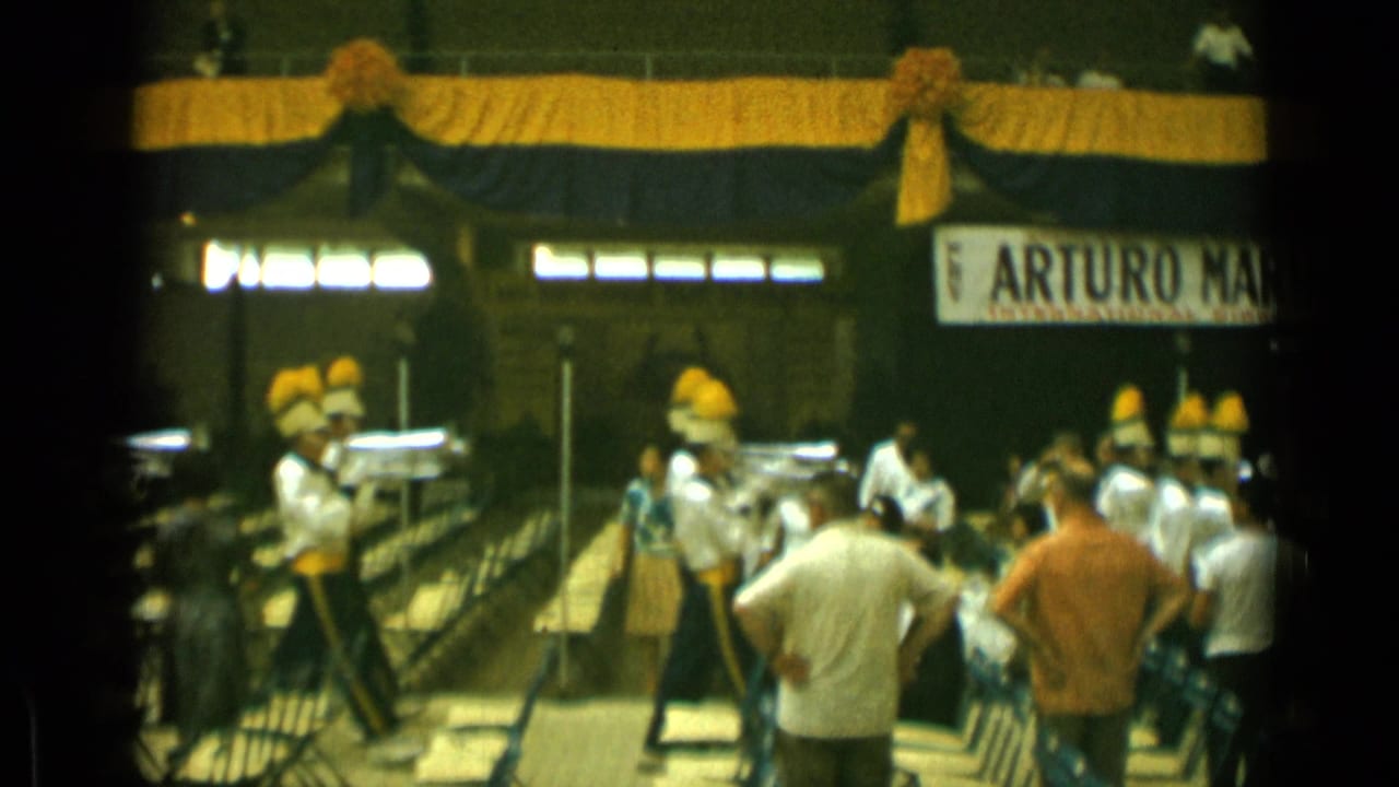 Uniformed musicians with tall yellow hats appear at a Cannes public event, with spectators seated near railings and partial signage behind them.
