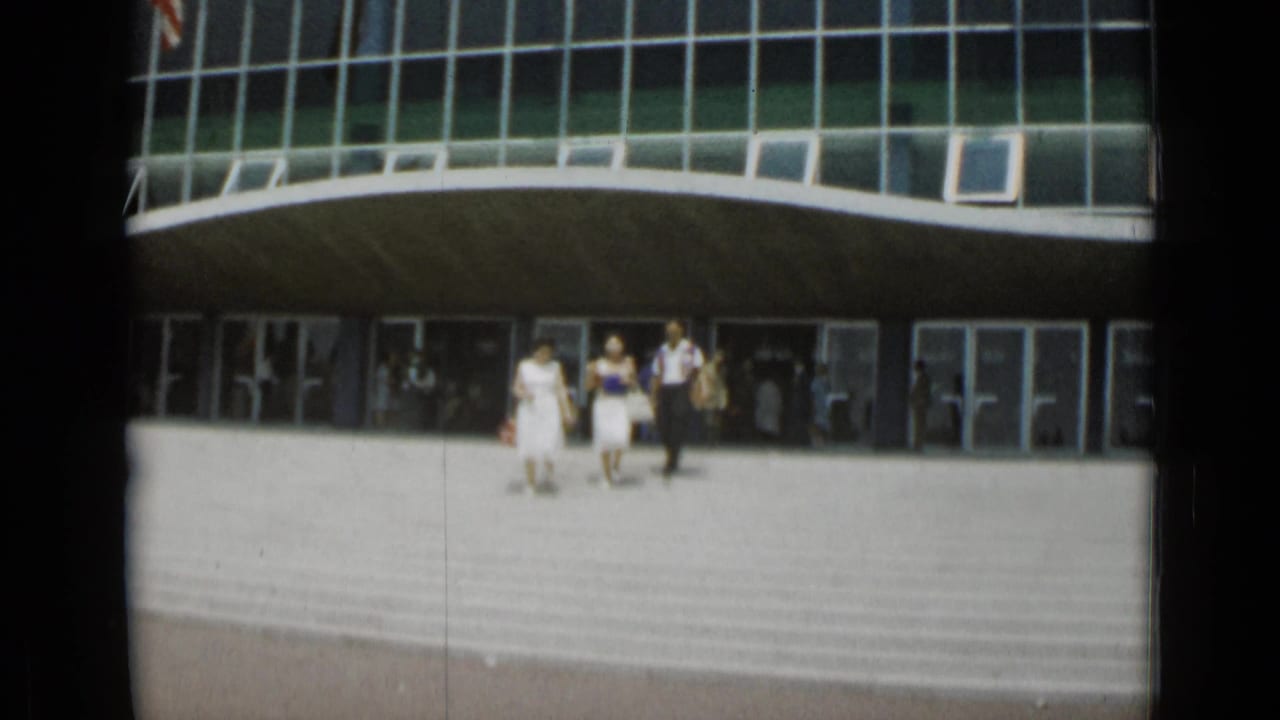Three adults descend wide steps outside a curved glass-fronted building.