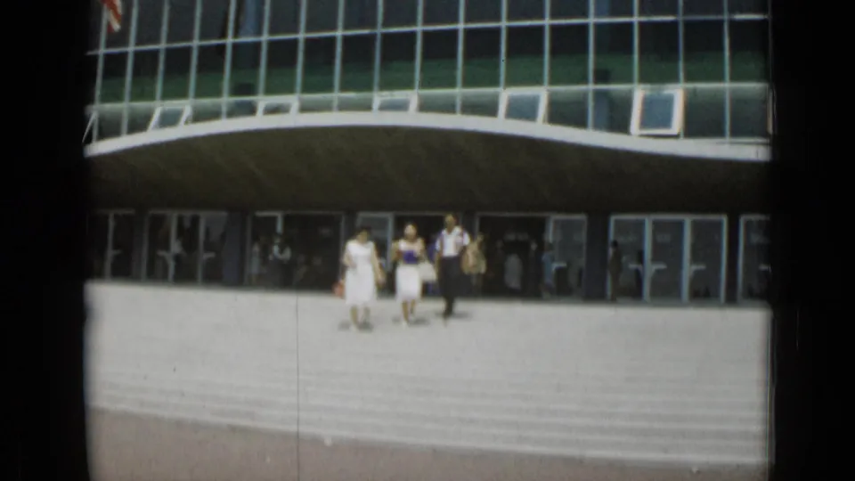 In Cannes, France in 1962, three adults walk down broad steps outside a modern building with a curved glass facade.