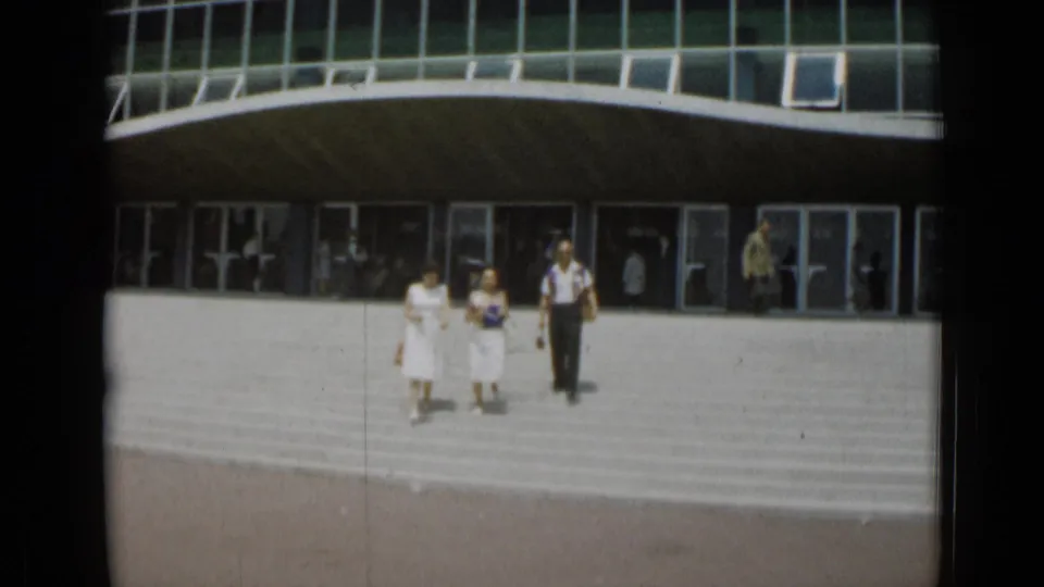 Two women in light dresses and a man in a light shirt and dark trousers descend the steps outside the Cannes building.
