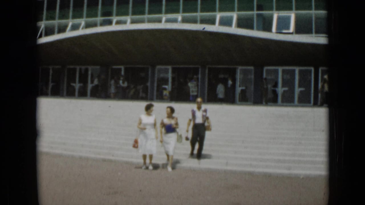 Three adults walk across a plaza in front of a curved glass building.