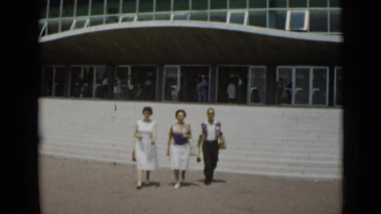 Two women and one man walk closer across a sunlit plaza.