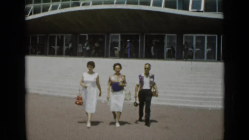 Two women in light clothing and a man in dark trousers walk across the plaza, with glass windows and steps behind them in Cannes.