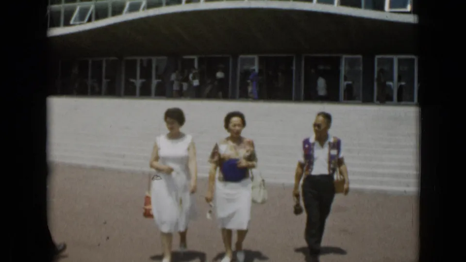 Near the end of the clip, the three adults are closer to the camera, walking past the curved modernist facade in Cannes, France.