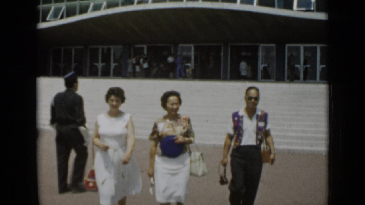 Three adults walk across a sunny parking area in front of a modern building.