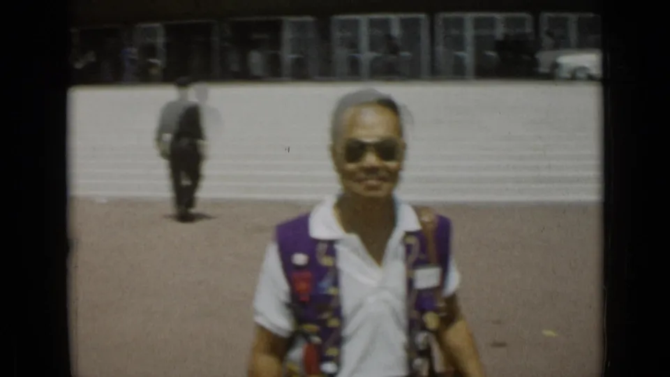 A man wearing sunglasses and a colorful vest stands close to the camera in the 1962 Cannes home-movie scene.