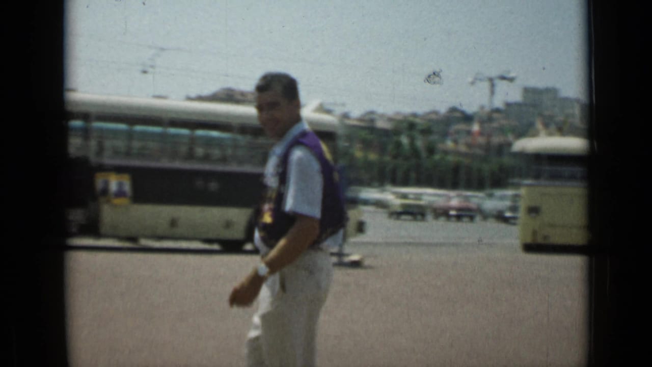 Man walking near the center of frame with a bus and distant cars in the background.
