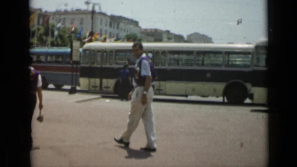 The 1962 Cannes street view shows a man in white trousers near a long bus, with international flags and pale buildings in the distance.