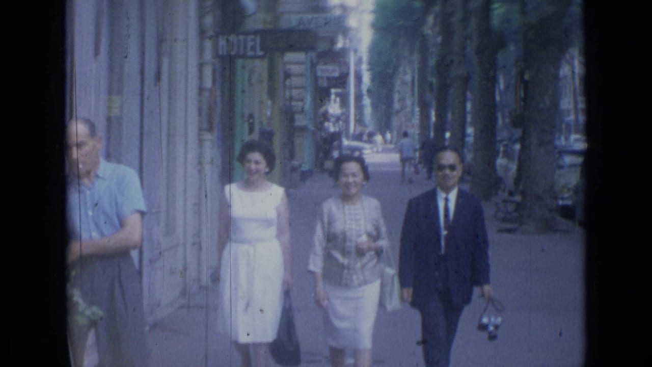 Three adults walk toward the camera on a tree-lined sidewalk with storefront signs behind them.