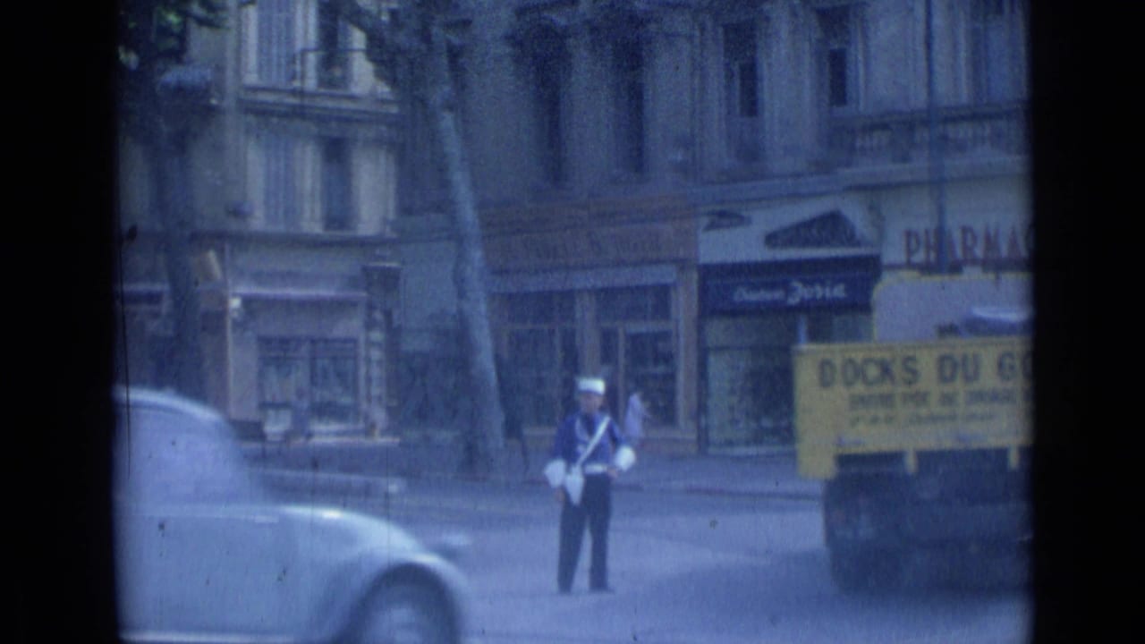 1962 Cannes street view with a traffic policeman in a white hat, cars, storefronts, and a yellow truck partly visible.